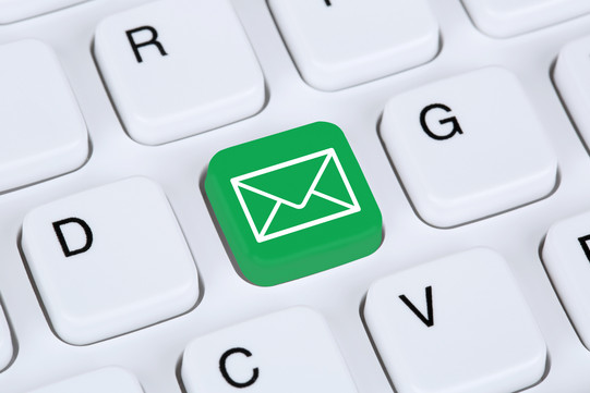 Email Eine weiße Tastatur im Detail. Eine Taste ist grün eingefärbt mit einem weißen Briefumschlag darauf.